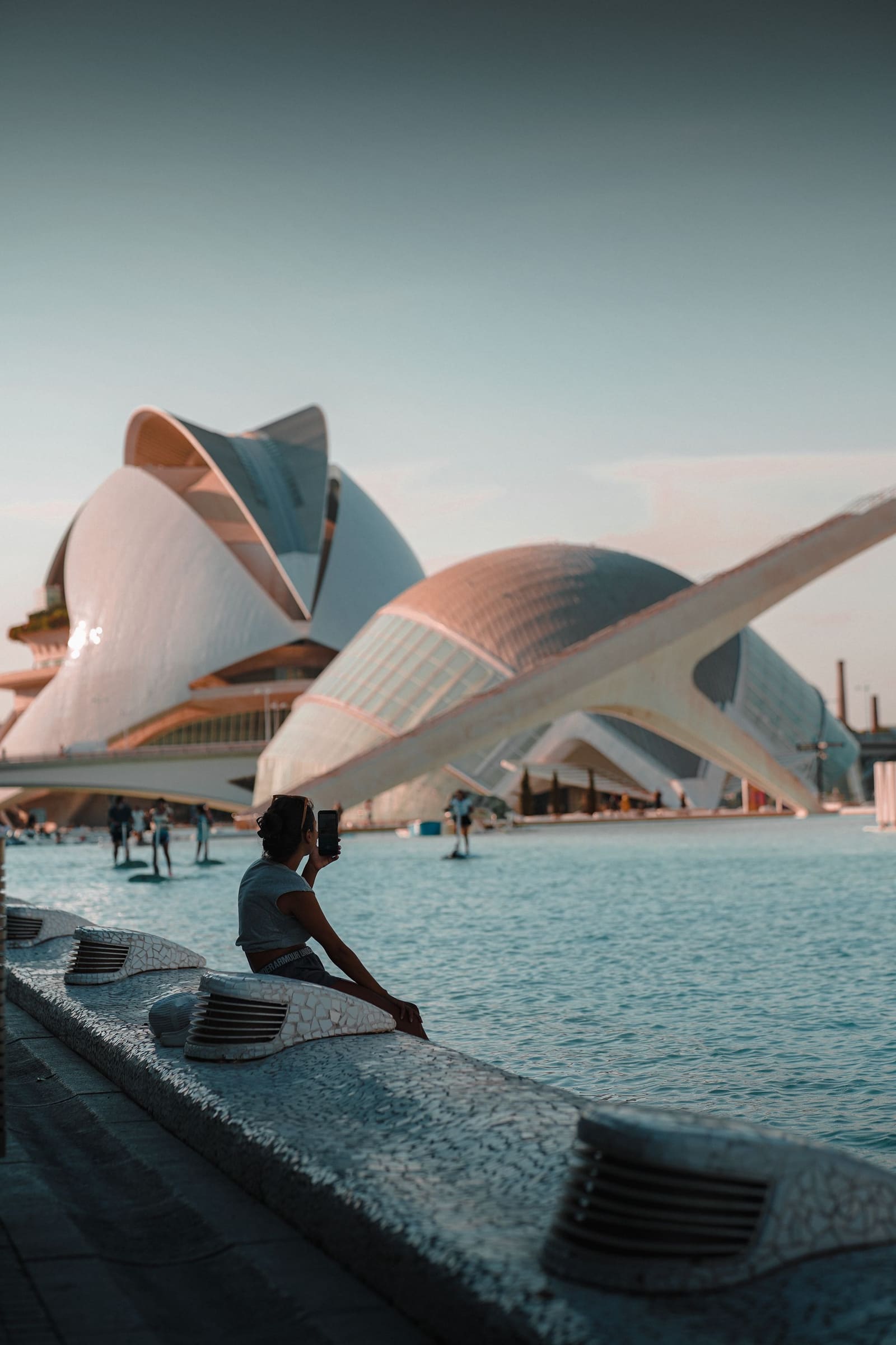 Una persona descansa junto al agua frente a la Ciudad de las Artes y las Ciencias